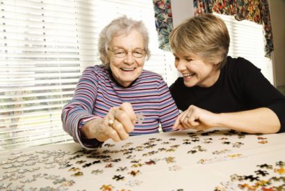 Opiekunka układa puzzle z seniorką i rozmawia po niemiecku.