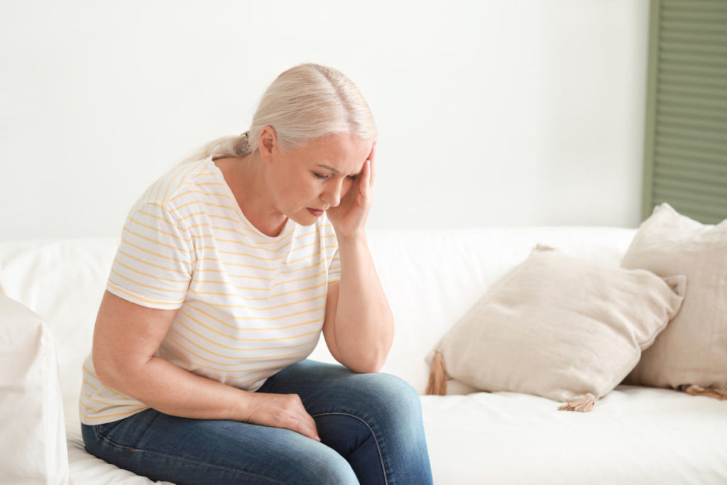 Chora opiekunka osoby starszej siedzi na kanapie z bolącą głową
