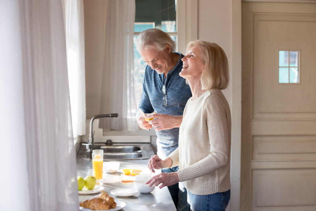 Opiekunka osoby starszej przygotowuje w kuchni śniadanie z mężem dla podopiecznego.